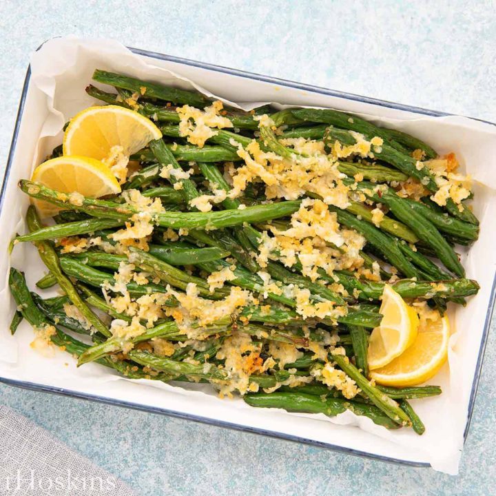 white tray with parmesan roasted green beans with lemon slices on the side.