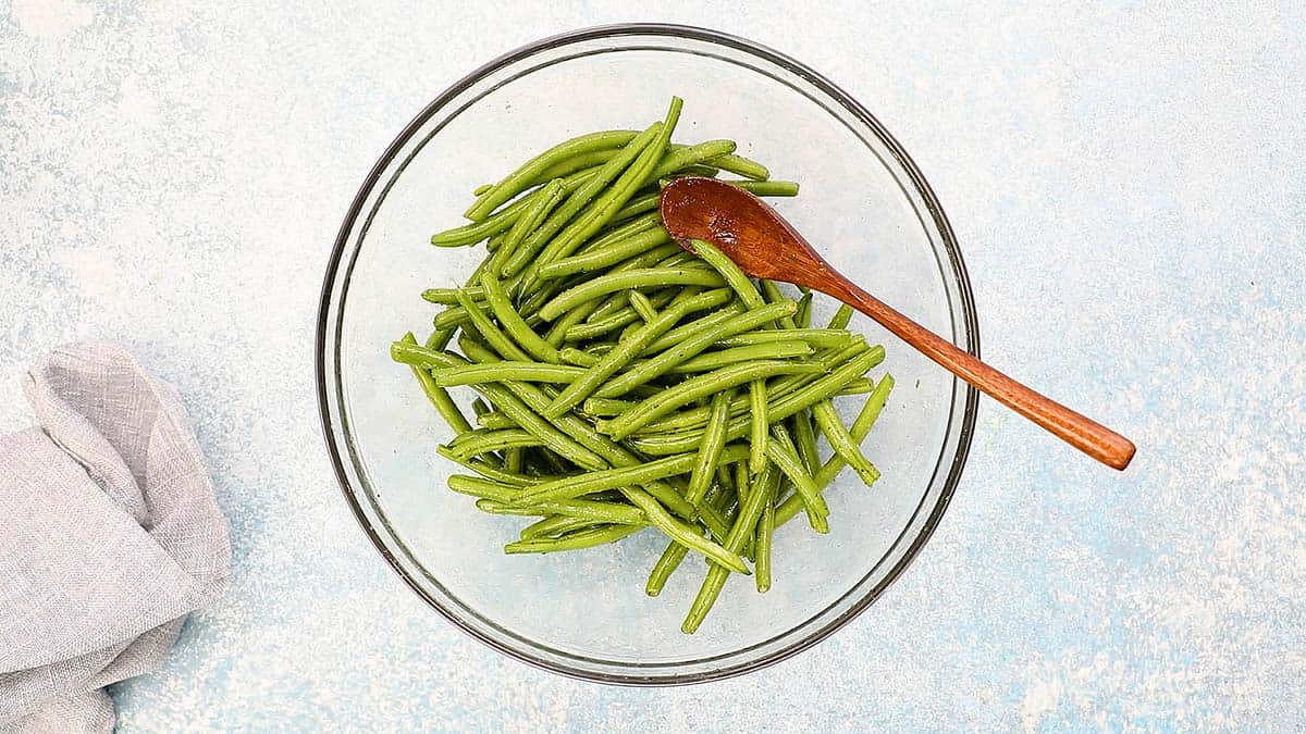 glass bowl with fresh green beans tossed with oil and seasoning.