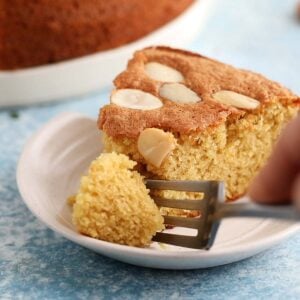 a hand cutting a piece from a cake slice using a fork.