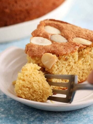 a hand cutting a piece from a cake slice using a fork.