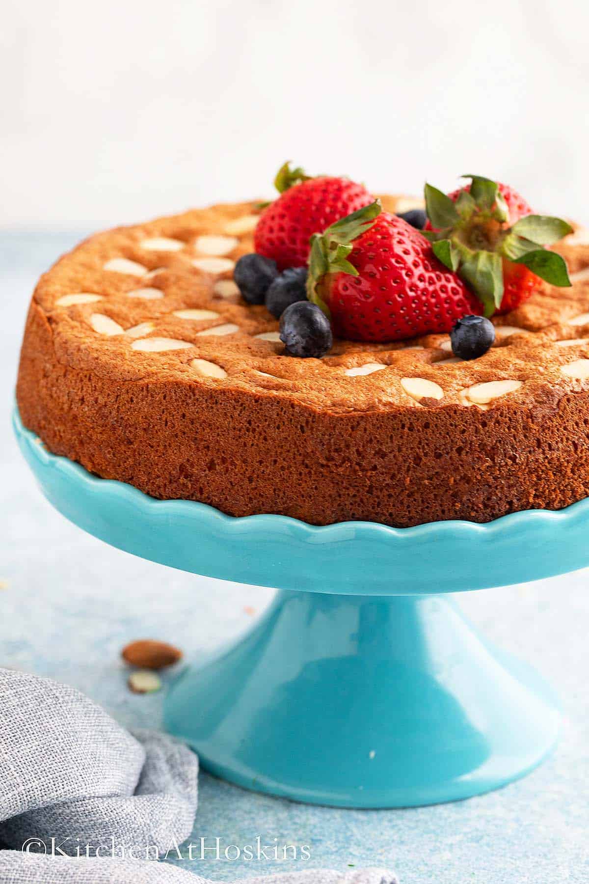 round almond cake on blue cake stand topped with berries.