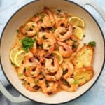 pink shrimp piled in a white skillet along with lemon slices.