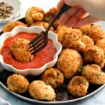 a hand dipping one breaded mushroom in red sauce placed in a white bowl.