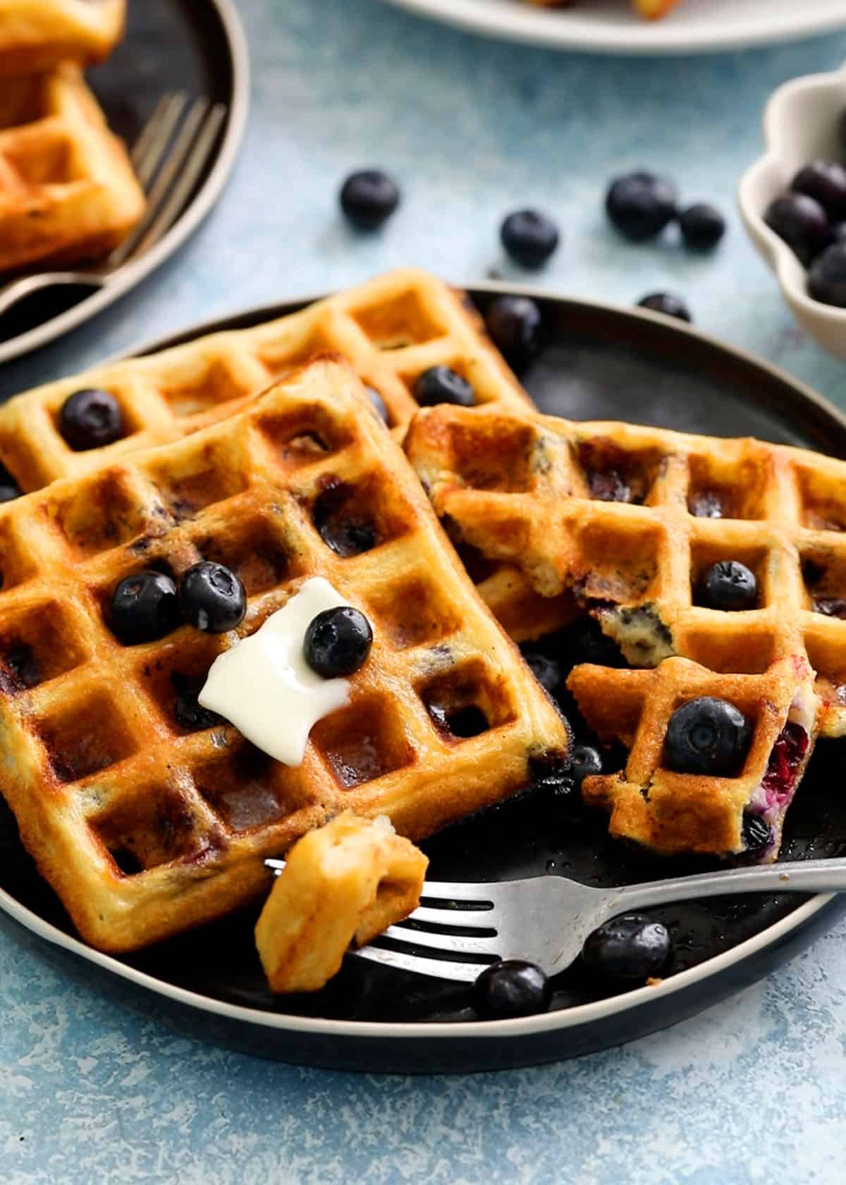 Three waffles topped with blueberries placed on a black plate.