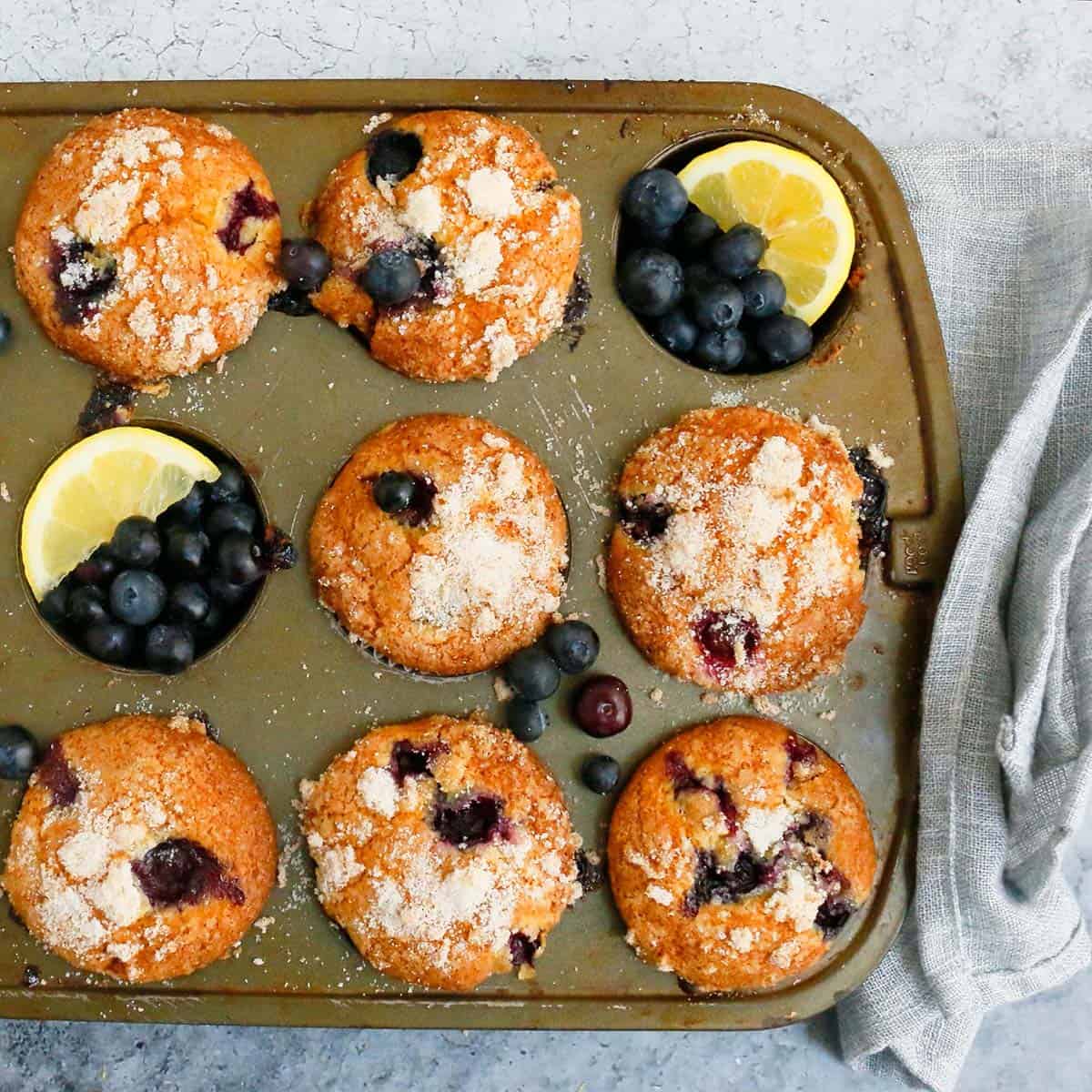 lemon blueberry muffins on a muffin pan garnished with blueberries and lemon slices