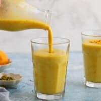 a hand pouring yellow colored mango milk into a drinking glass.