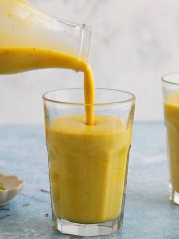 a hand pouring yellow colored mango milk into a drinking glass.