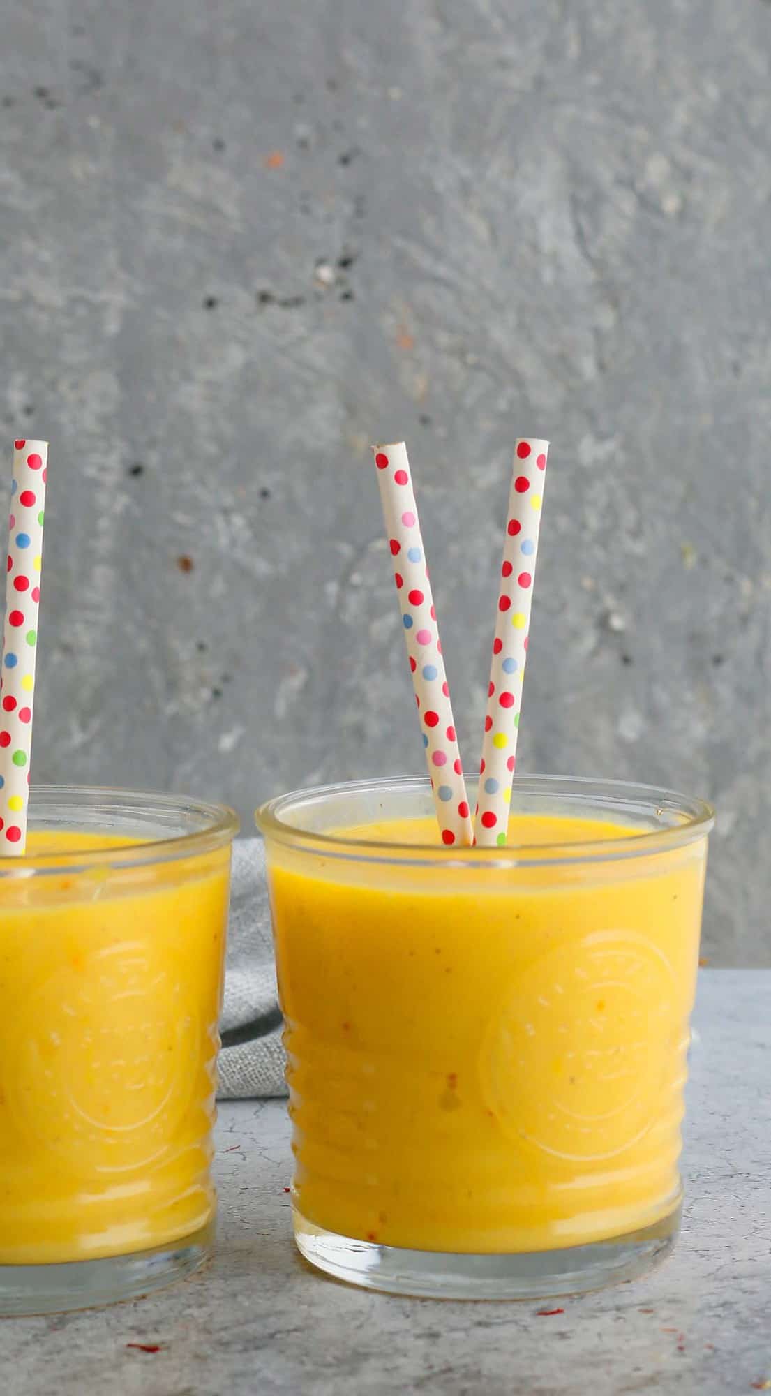 glasses filled with fresh mango milk along with polka dot straws