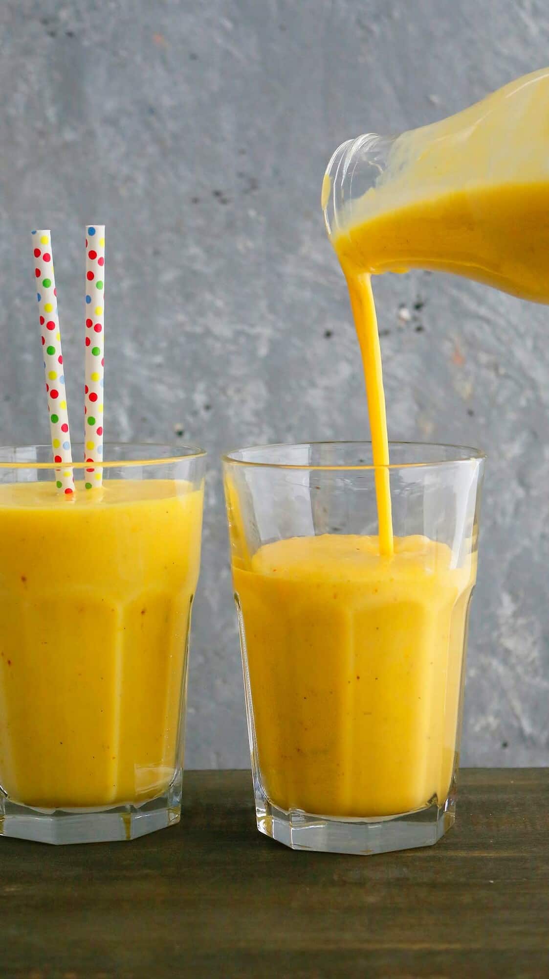 a hand pouring yellow milk into a drinking glass.