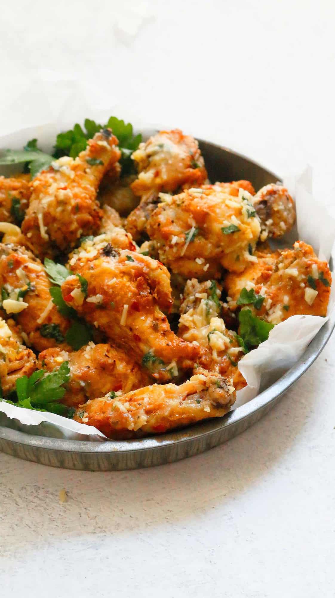  parchment lined round metal tray with garlic parmesan wings, garnished with parsley