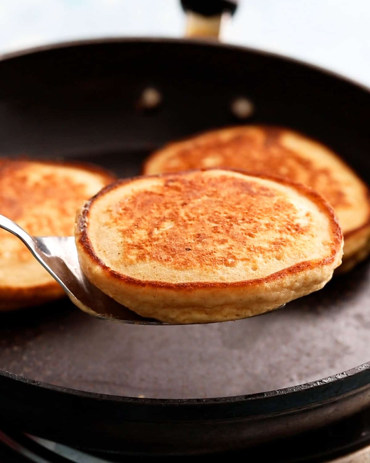 a hand lifting one round pancake from a black skillet.