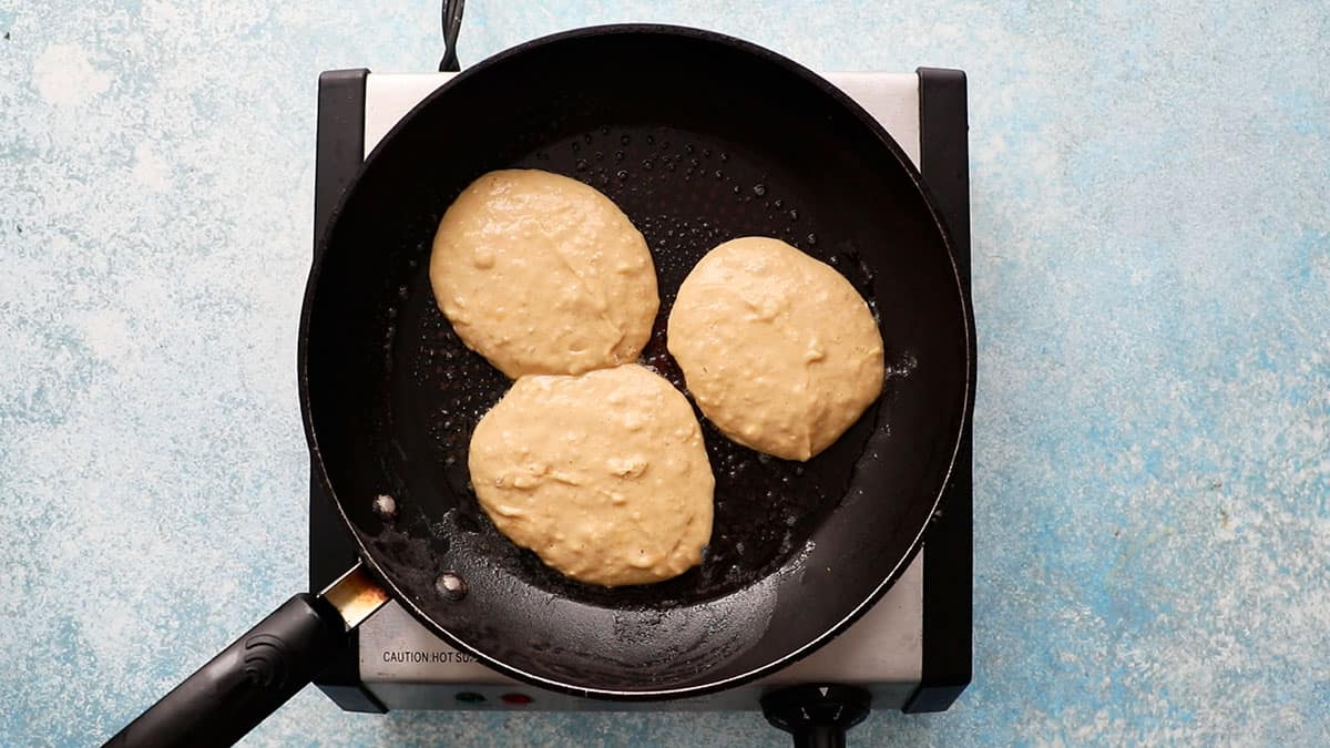 three pancakes cooking in a black skillet.