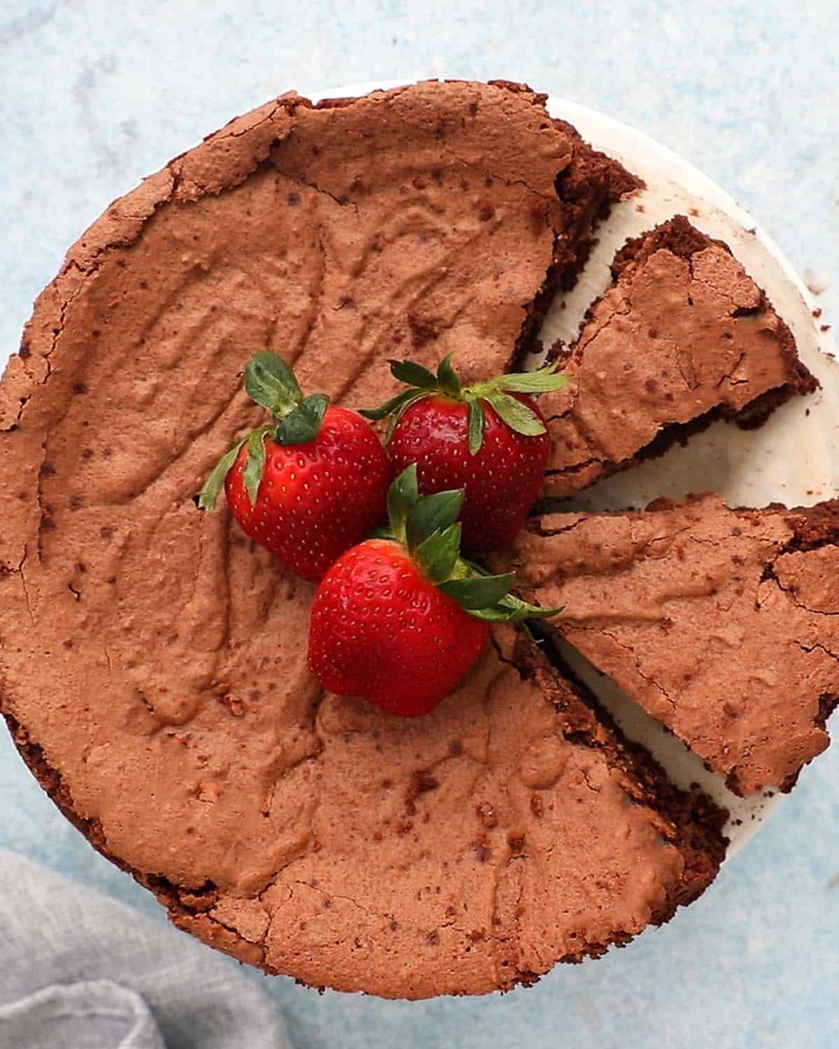 sliced chocolate cake topped with 3 strawberries, on a white cake stand. 