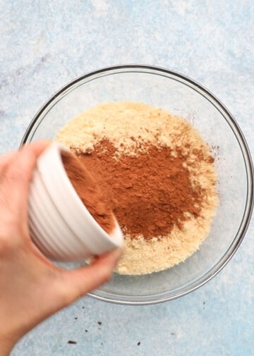 a hand adding cocoa powder into a glass bowl.