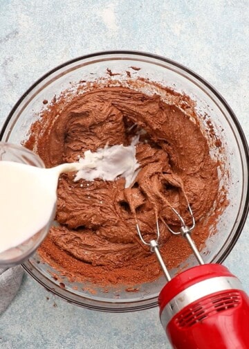 a hand pouring milk into a glass bowl with brown cake batter.
