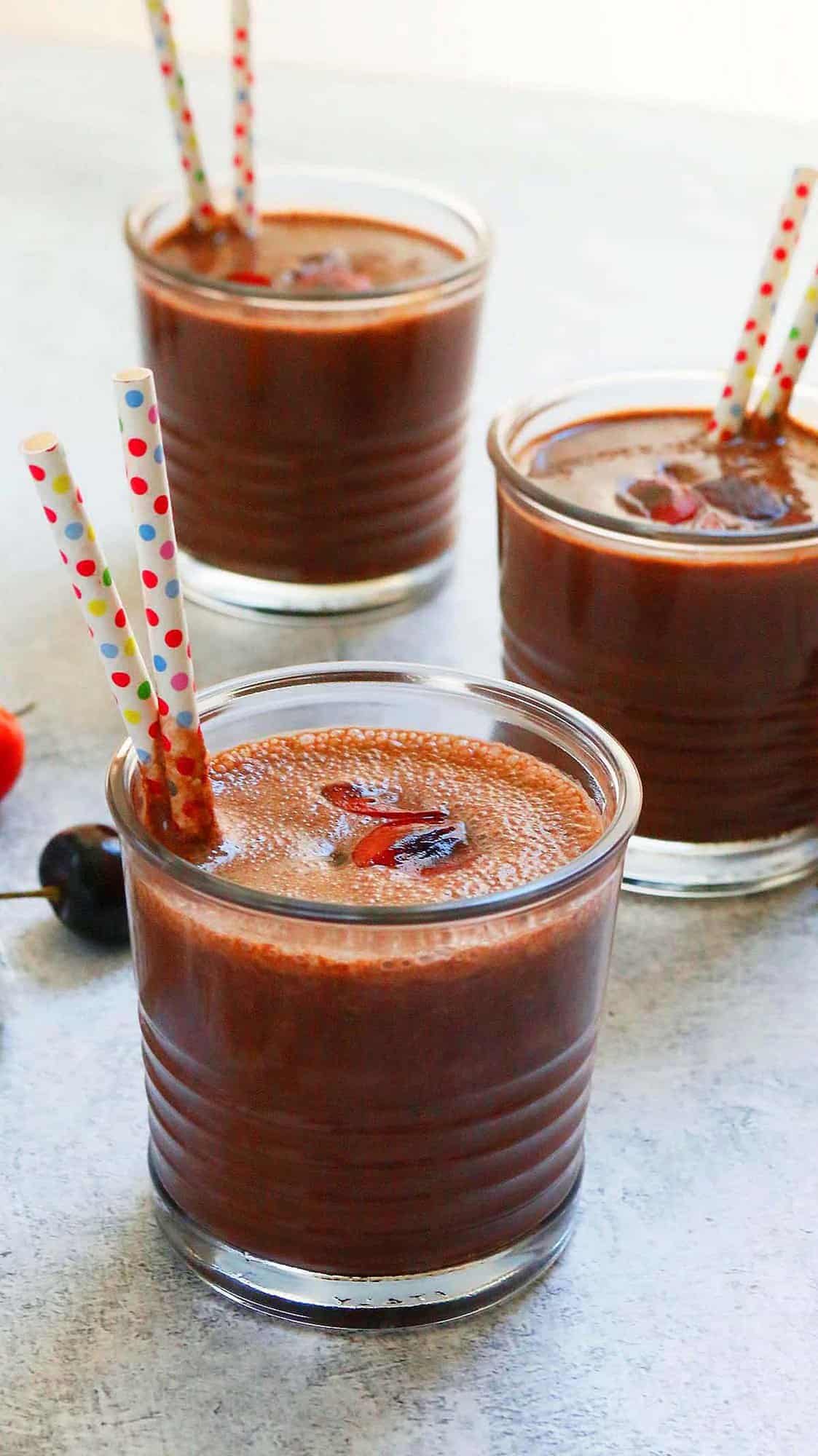 3 glasses filled with chocolate smoothie topped with cherries.