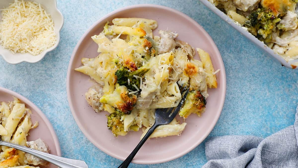 white chicken, broccoli, pasta in a round pink plate along with a black fork.