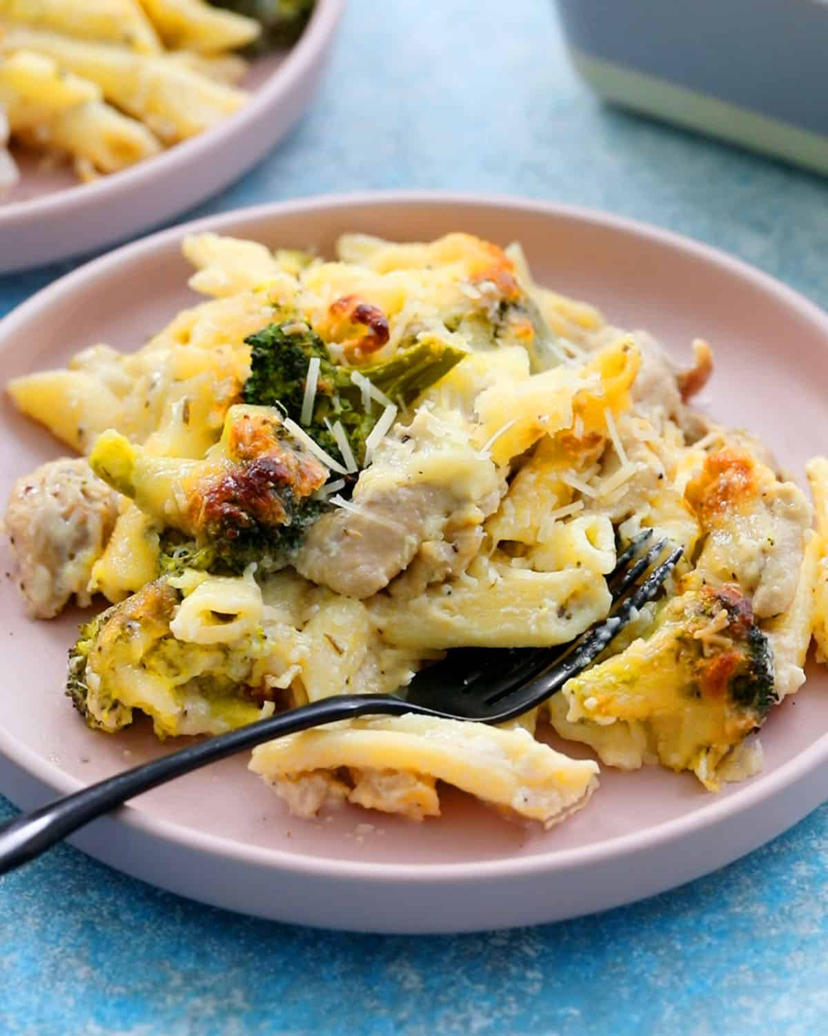 white chicken, broccoli, pasta in a round pink plate along with a black fork.