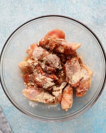 raw chicken wings with spices sprinkled over them in a glass bowl.