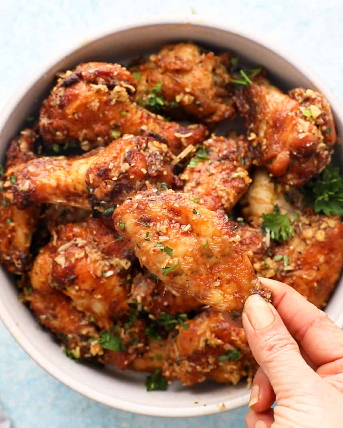 a hand holding one cooked brown chicken wing.