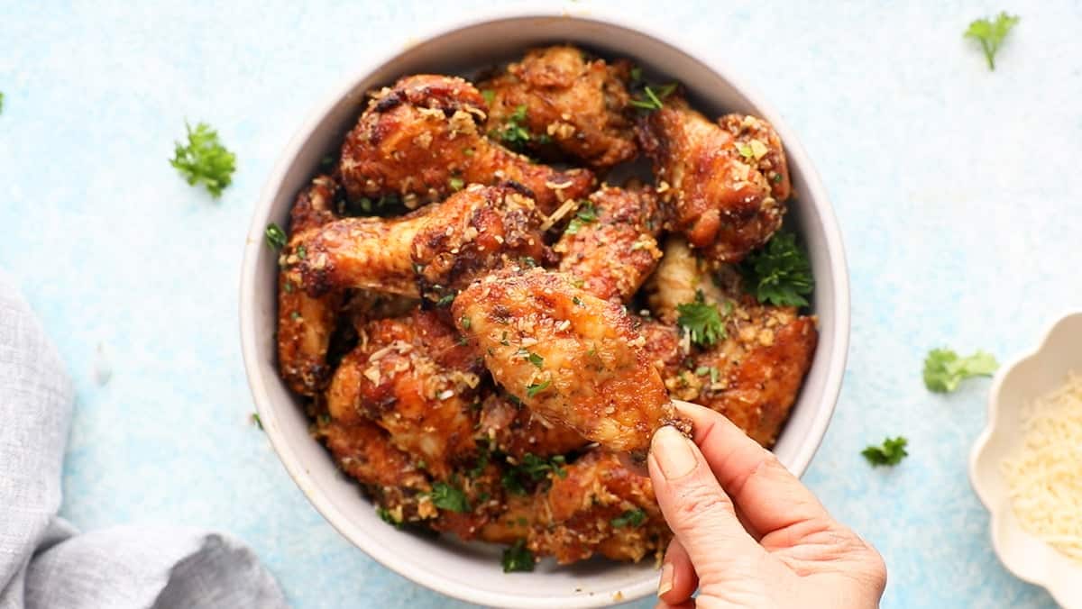 a hand holding one cooked brown chicken wing.