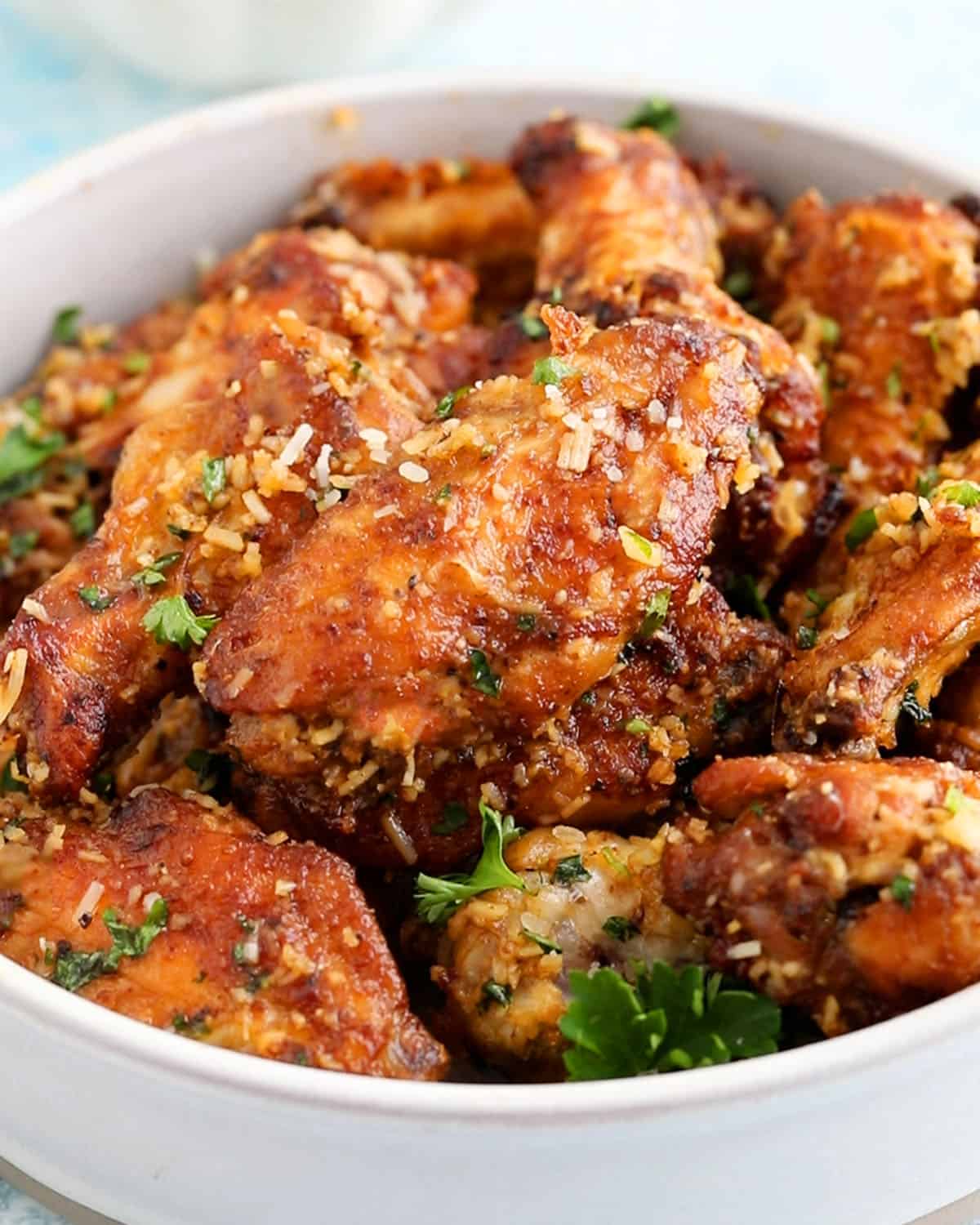 a large white bowl filled with brown garlic parmesan wings.