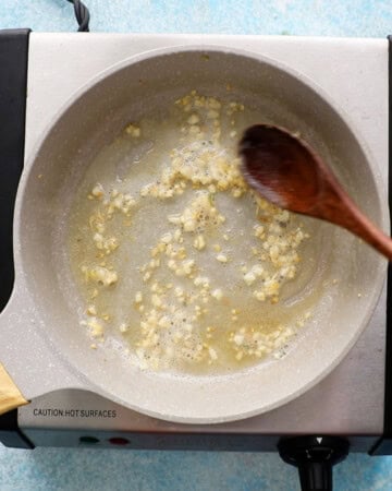 chopped garlic cooking in melted butter in a small white skillet.