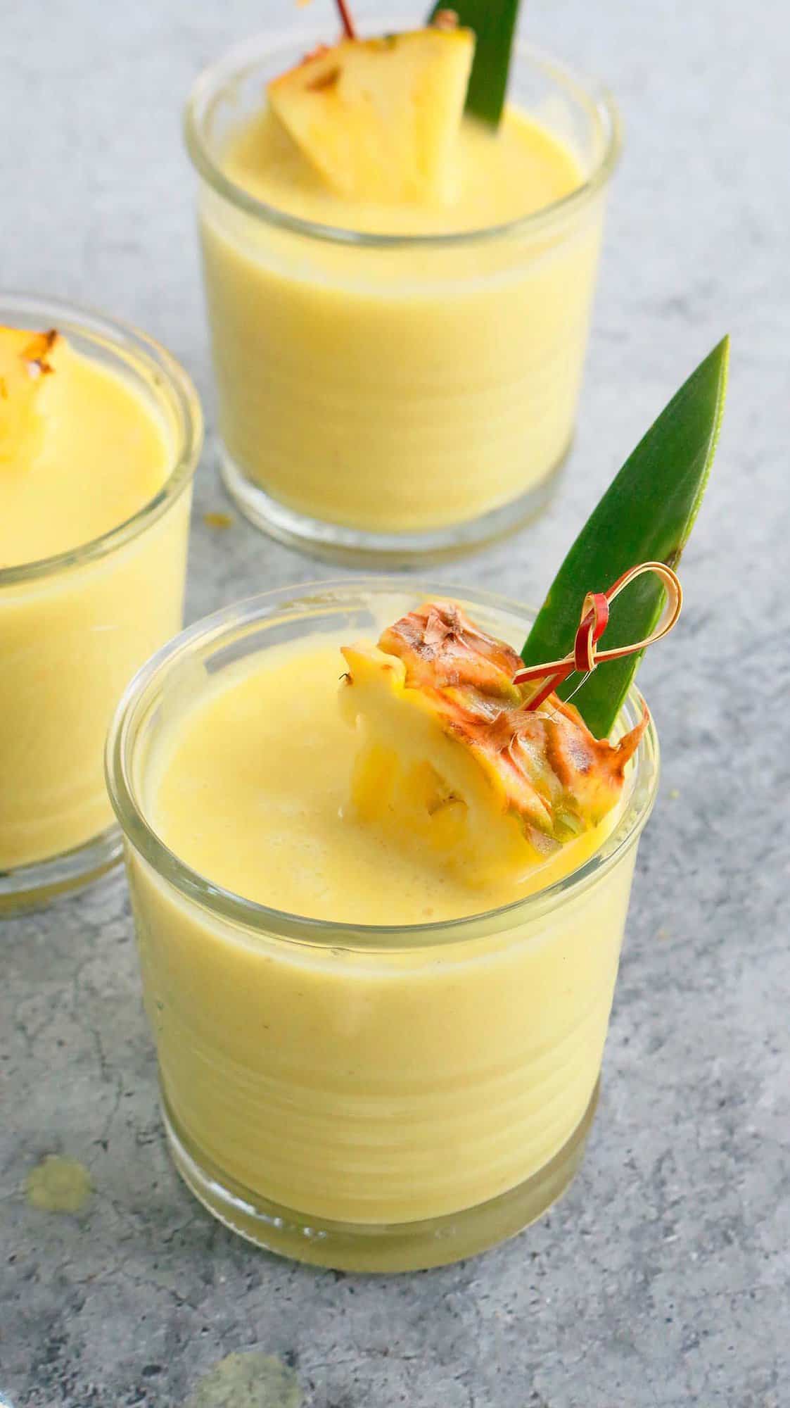 3 glasses with yellow smoothie garnished with pineapple. 