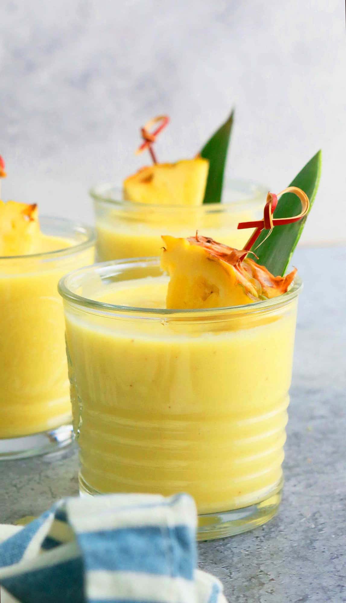 3 glasses with yellow smoothie garnished with pineapple chunks.