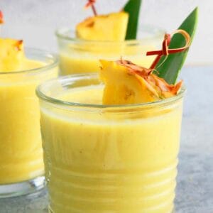 3 glass tumblers with yellow smoothie and garnished with pineapple.