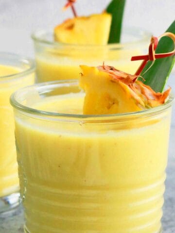 3 glass tumblers with yellow smoothie and garnished with pineapple.