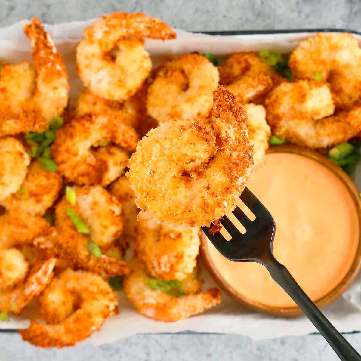 fork holding a crispy shrimp above a platter filled with more shrimp