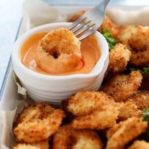a cooked breaded shrimp dipped into a pink sauce using a fork.