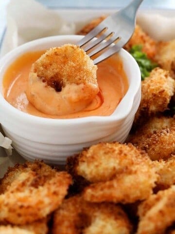 a cooked breaded shrimp dipped into a pink sauce using a fork.