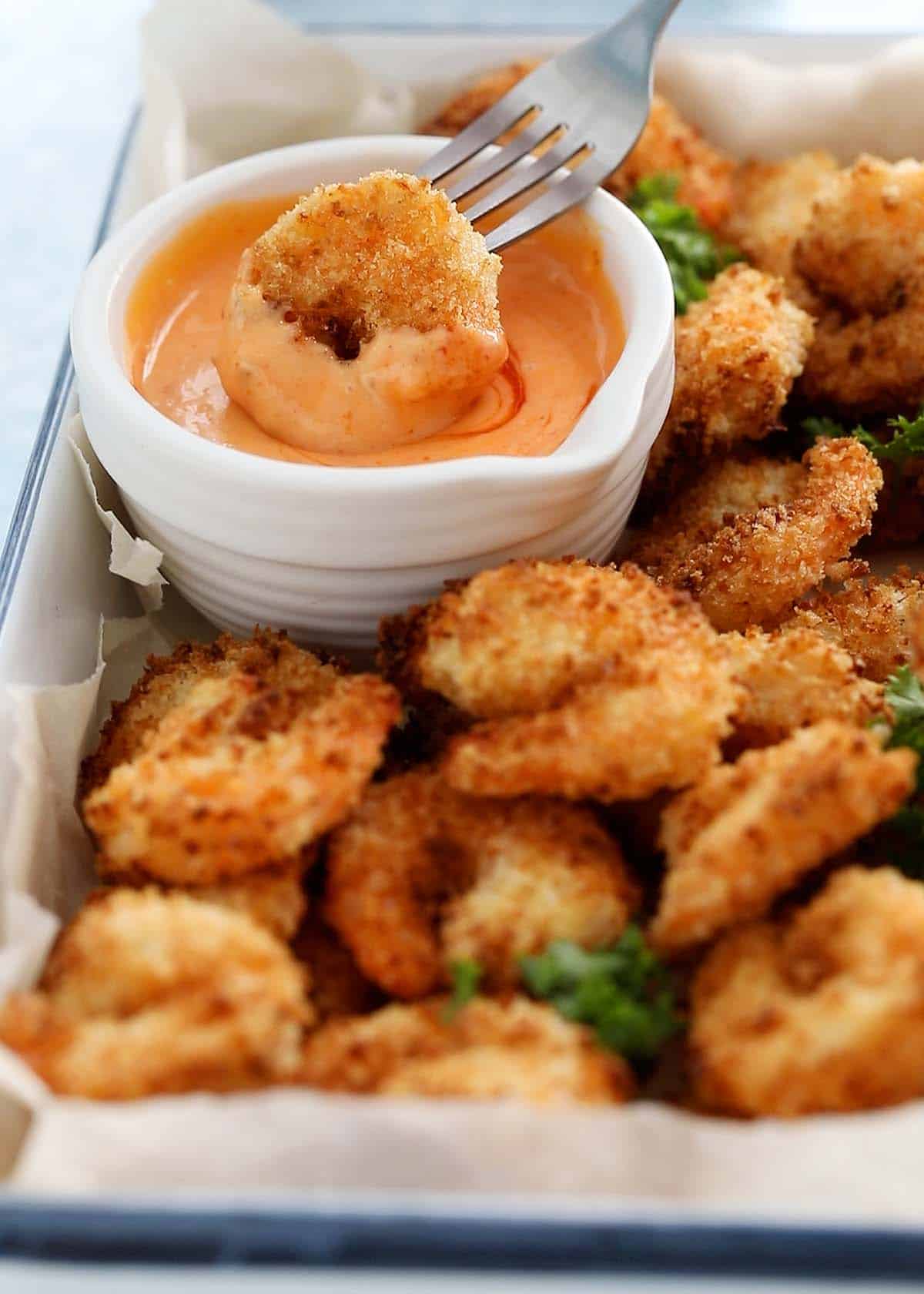 a cooked breaded shrimp dipped into a pink sauce using a fork.