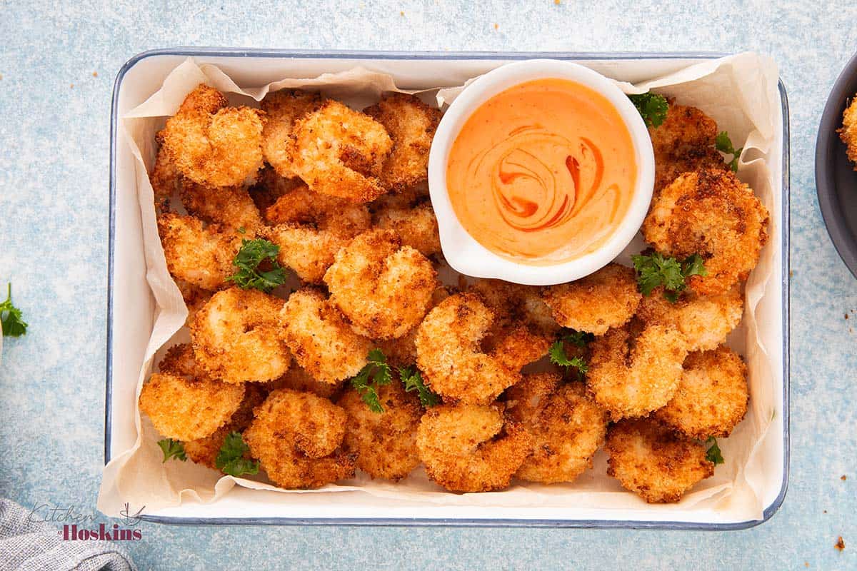 a rectangular white tray with cooked shrimp and a white bowl with orange sauce. 