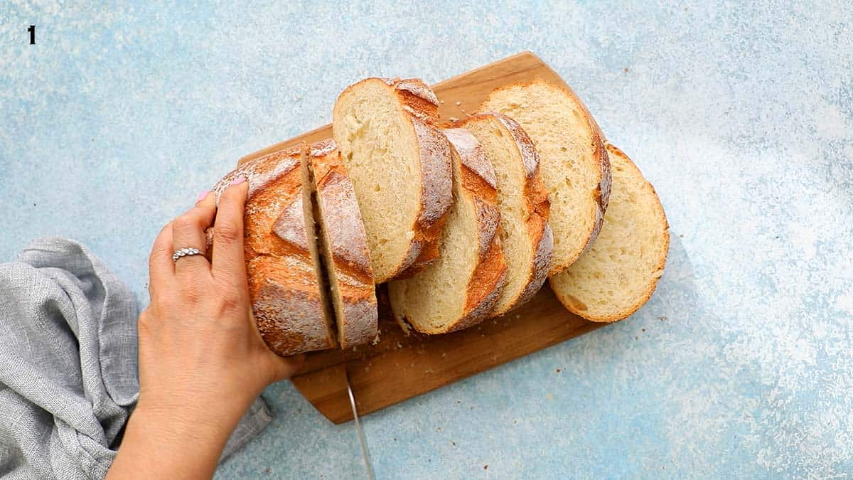 two hands slicing a loaf of bread on a wooden board.