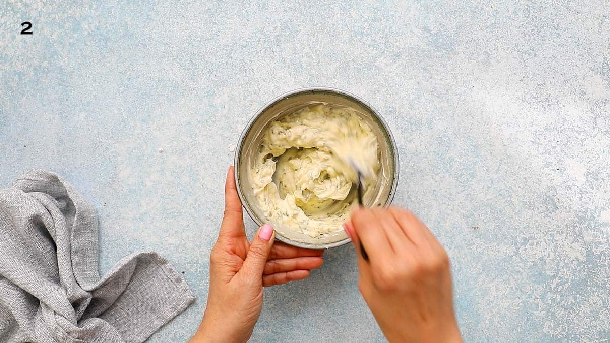 two hands mixing garlic butter in a blue bowl.