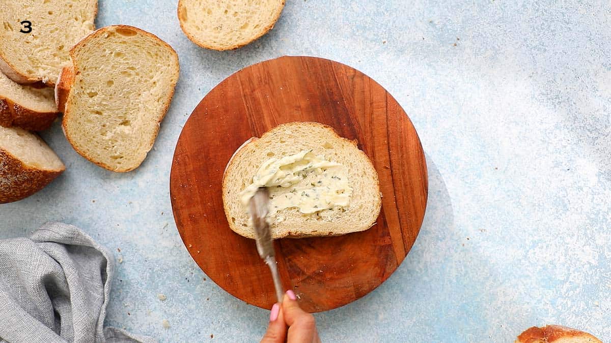 two hands spreading garlic butter on a sliced bread.