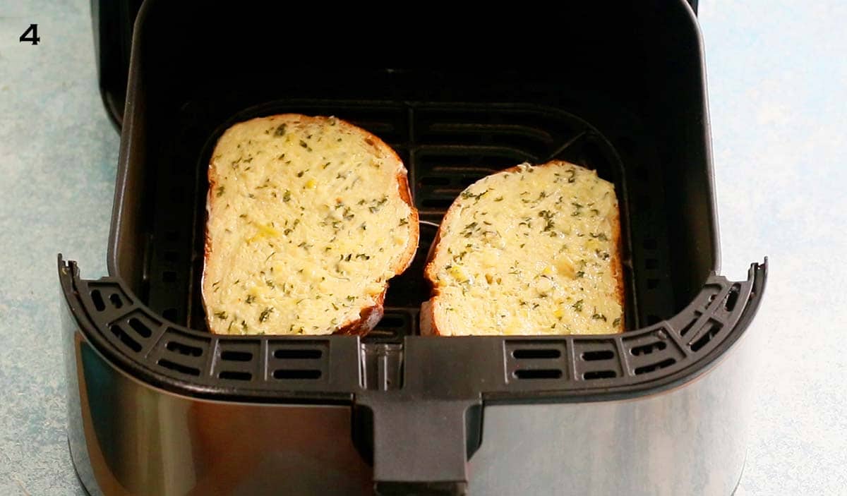 two slices of bread with garlic butter placed in an air fryer basket.