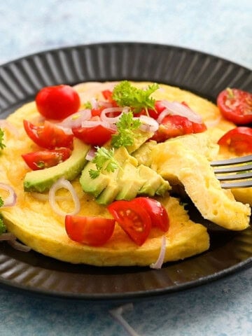 one round omelette topped with tomatoes and avocado.