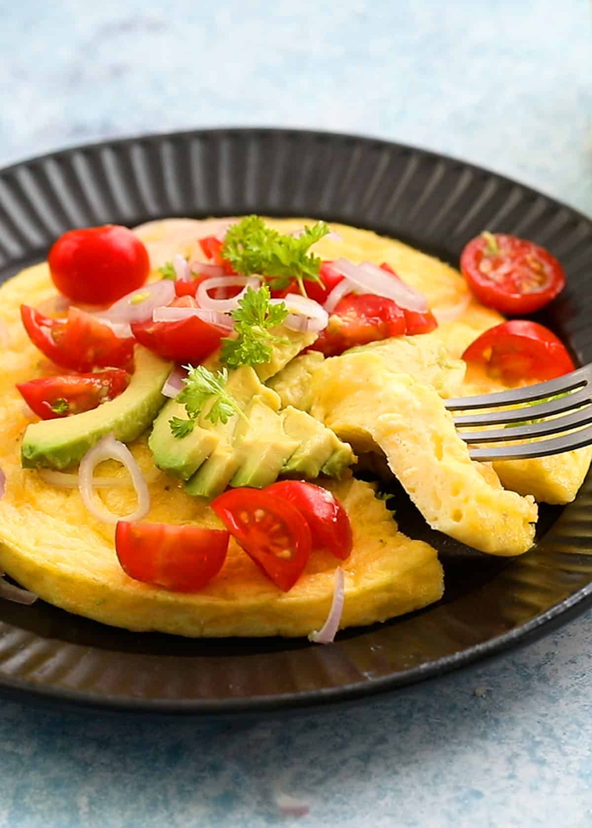 one round omelette topped with tomatoes and avocado in a black plate.