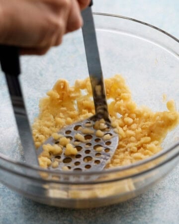 a hand mashing bananas in a glass bowl.