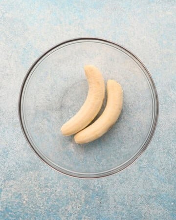 two peeled bananas in a glass bowl.