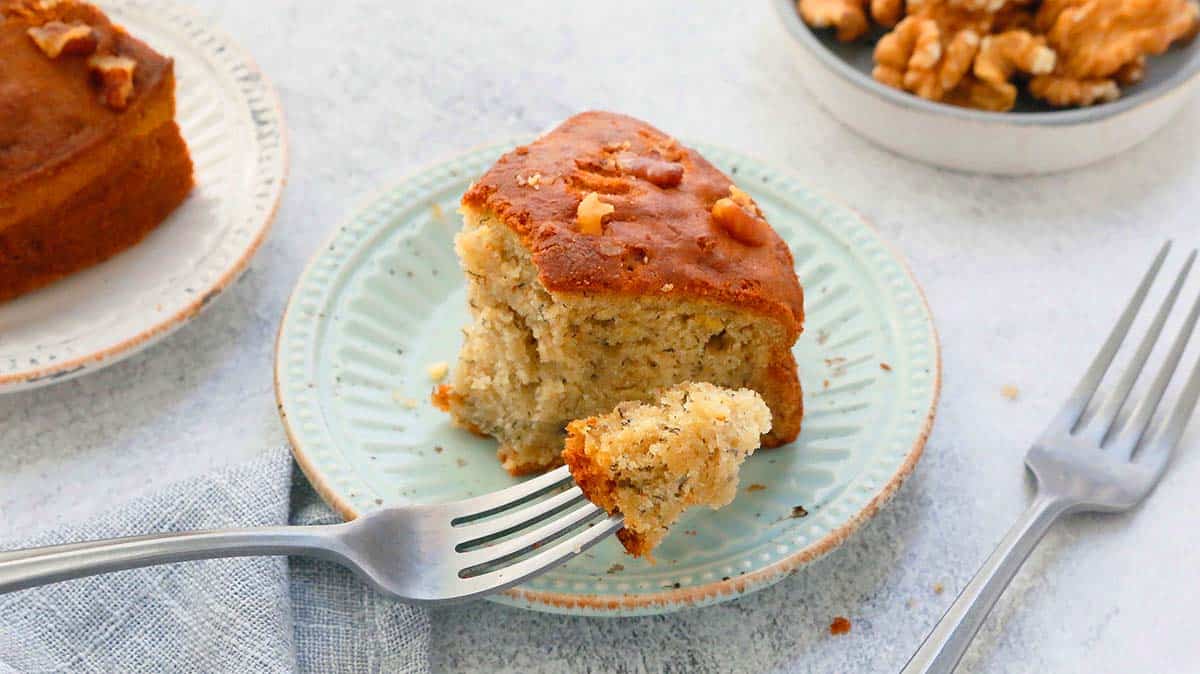 a slice of cake in a green plate along with a fork holding a bite.