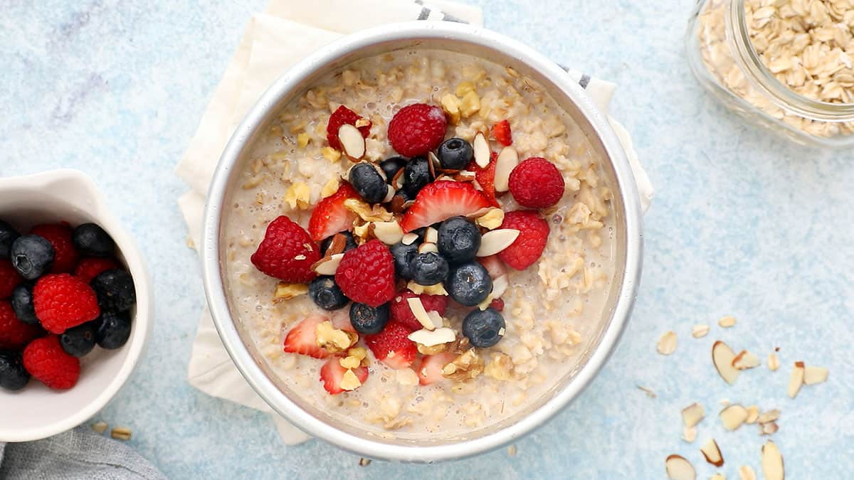 cooked oatmeal topped with berries in a round white metal pan.