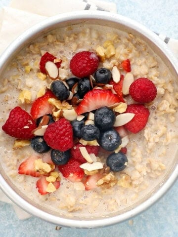 cooked oatmeal topped with fresh berries in a round metal pan.