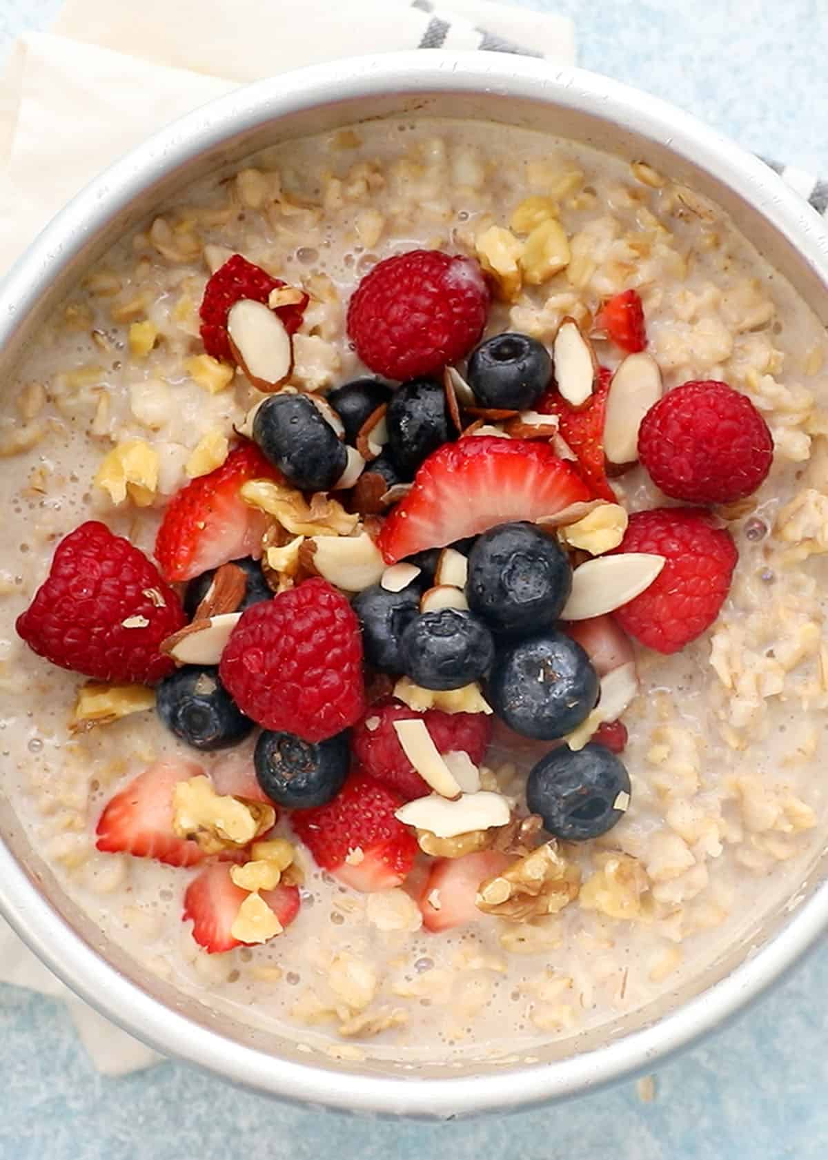 cooked oatmeal topped with berries in a round white metal pan.