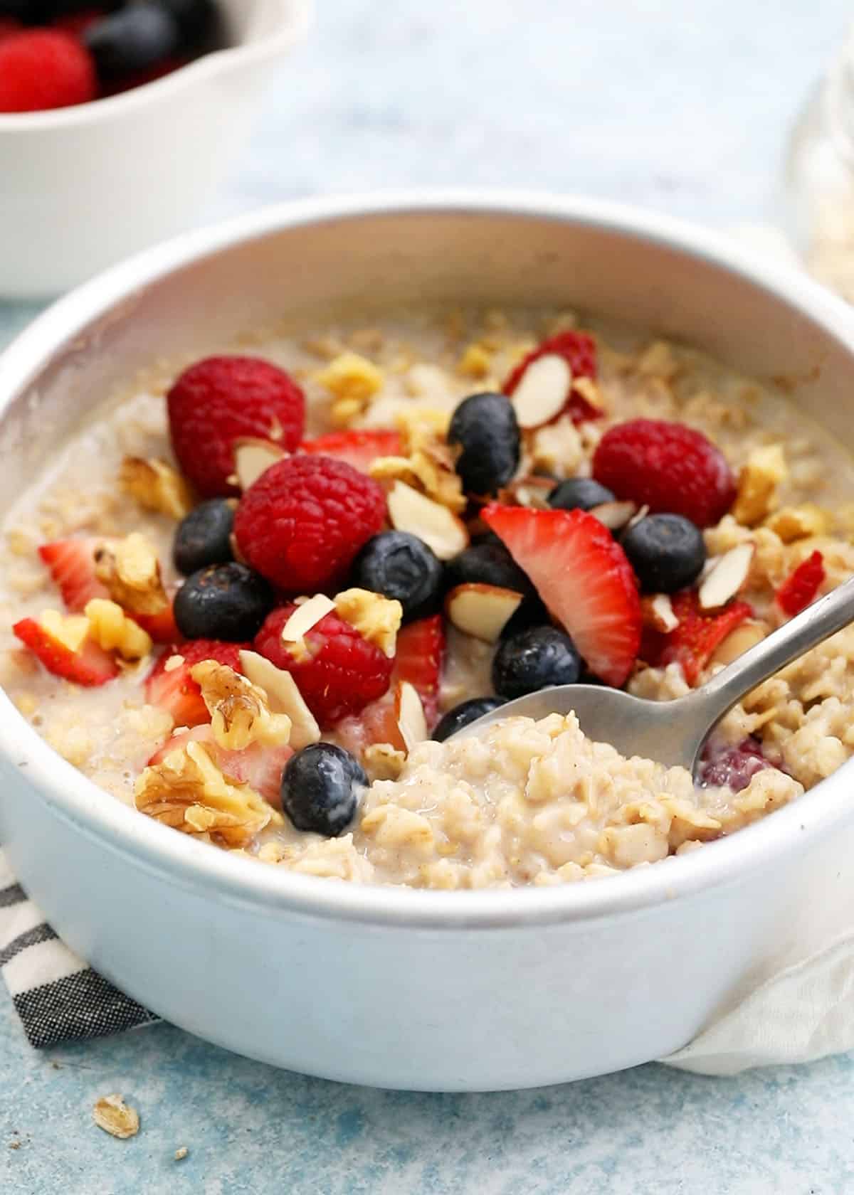 cooked oatmeal topped with berries in a round white metal pan.