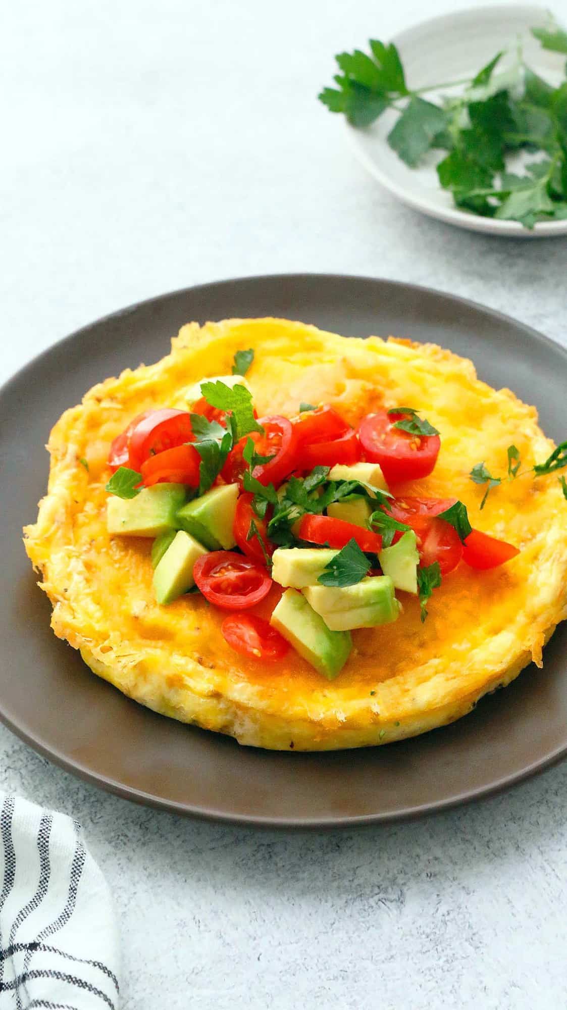 egg omelette topped with tomato and avocado on a brown plate 